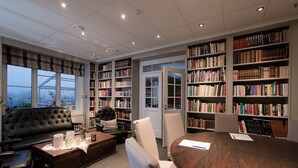 A library with bookshelves, a leather sofa, a wooden coffee table, and a round table with papers. - Nermo Hotell (Øyer)