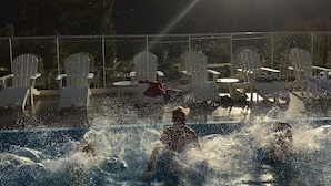 A swimming pool with people enjoying the water, surrounded by white lounge chairs and a scenic view of hills in the background. - Nermo Hotell (Øyer)