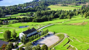 A golf course with a clubhouse, a parking area, and surrounding green fields. - Nermo Hotell (Øyer)