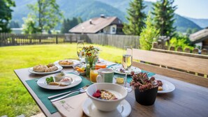 A breakfast table set outdoors with plates of food, a bowl of cereal, and a glass of juice. - Ski- & Wanderhotel Berghof (Bad Kleinkirchheim)