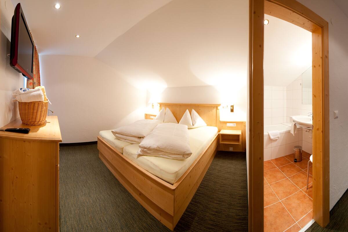 Une chambre avec un lit en bois, une table de chevet avec un panier, une télévision et une salle de bain avec un lavabo et un miroir.