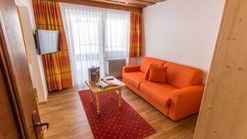 A cozy living room with a wooden ceiling, a red polka dot rug, an orange sofa, and a flat-screen TV mounted on the wall.