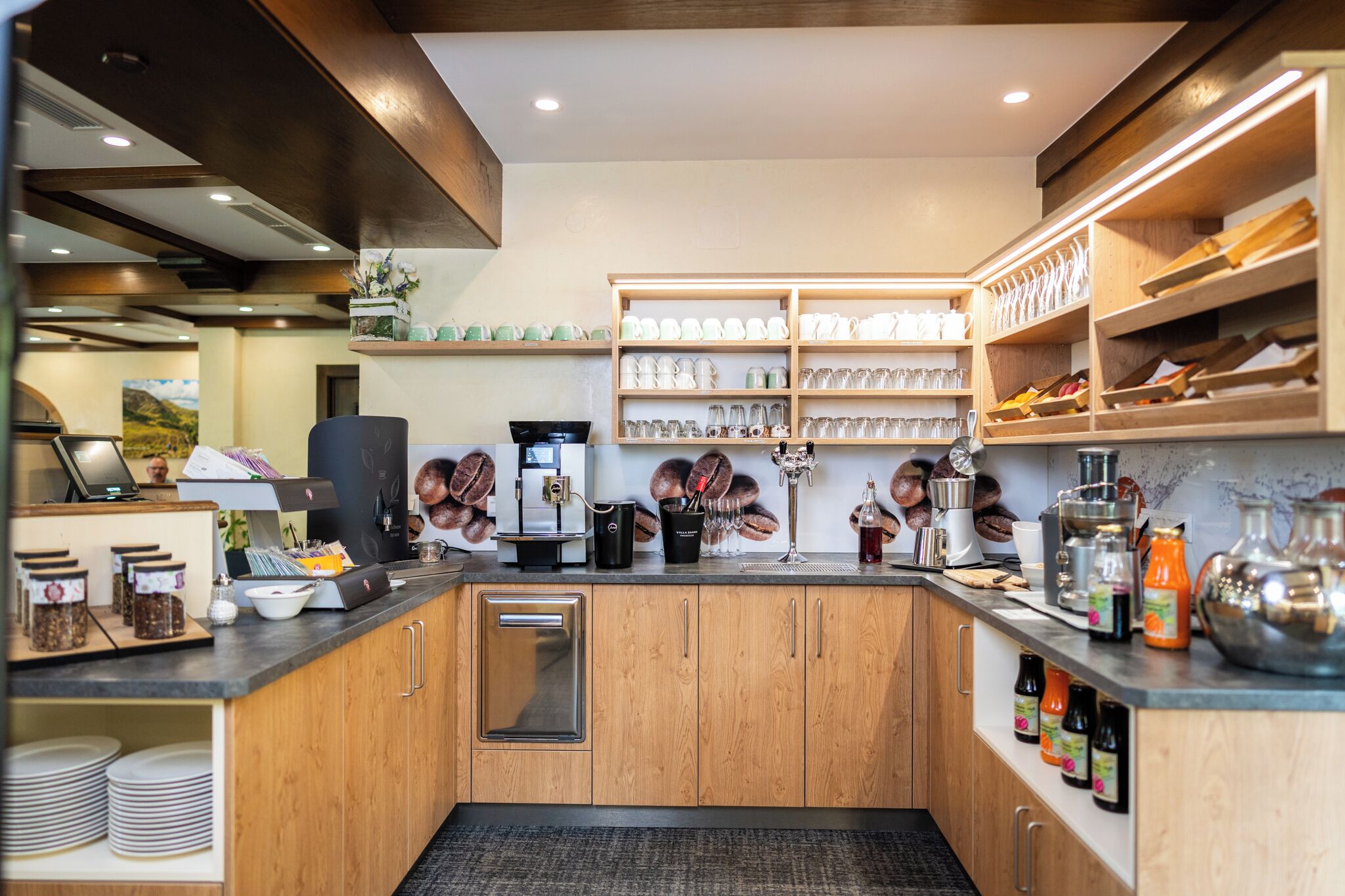 A modern kitchen with wooden cabinets, stainless steel appliances, and neatly organized shelves with glassware and jars.