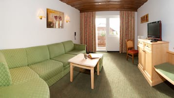 Una habitación acogedora con un sofá verde, una mesa de madera, un televisor sobre un mueble de madera y vistas a un edificio a través de la ventana.