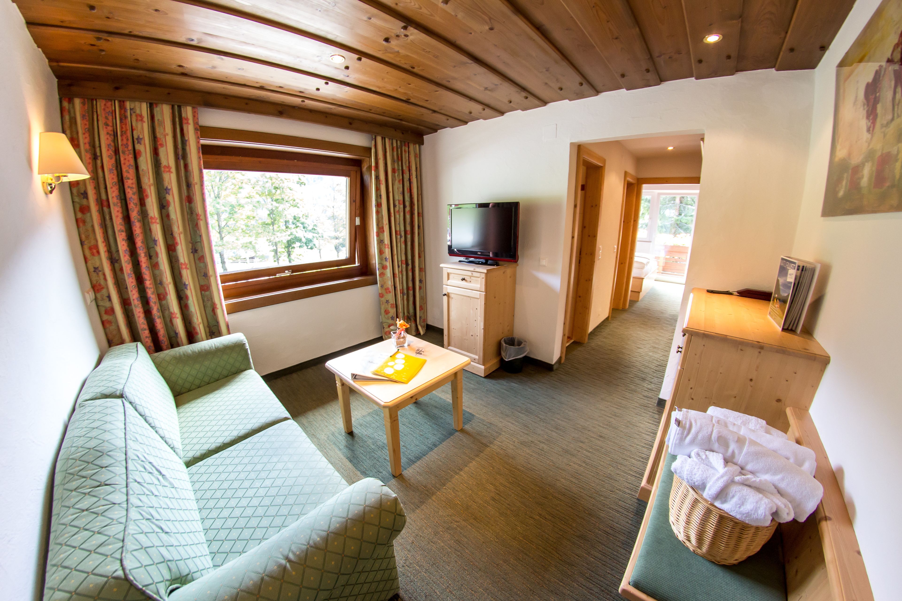 A cozy room with a sofa, a small table, a television, and a wooden cabinet with towels.
