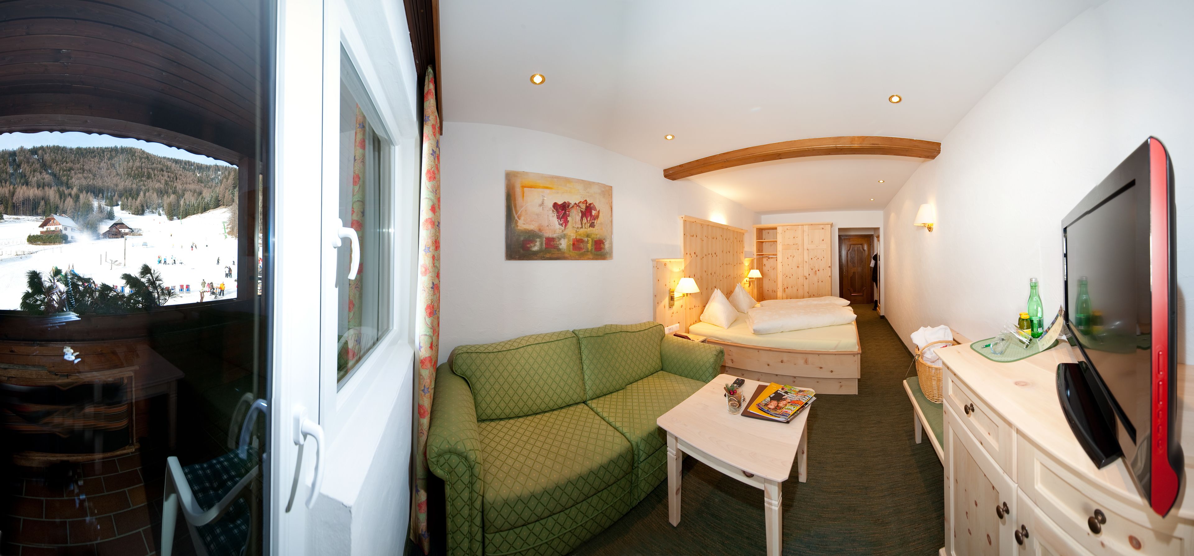 Une chambre d’hôtel avec un canapé vert, un lit en bois, une télévision et un tableau au mur.
