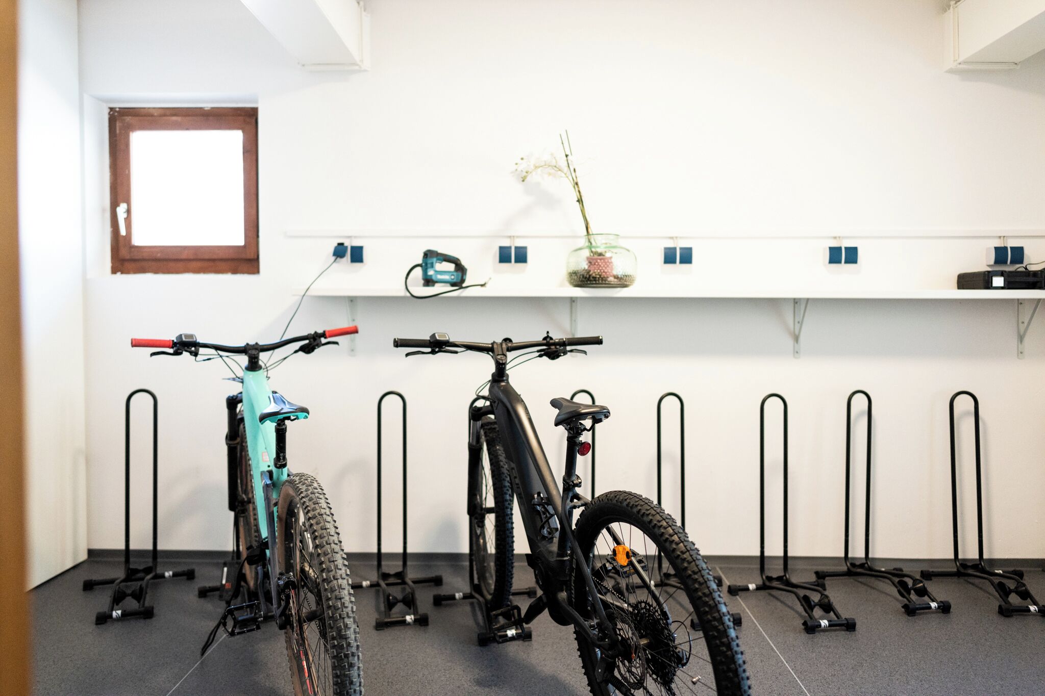 A room with two bicycles parked against a wall, a window, and a shelf with various items.