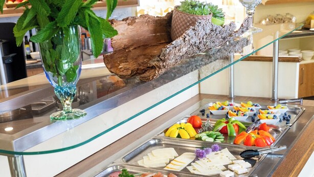 A buffet with various food options, a glass display case with plants, and a plate with butter. - Ski- & Wanderhotel Berghof (Bad Kleinkirchheim)