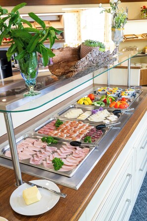 A buffet with various food options, a glass display case with plants, and a plate with butter. - Ski- & Wanderhotel Berghof (Bad Kleinkirchheim)