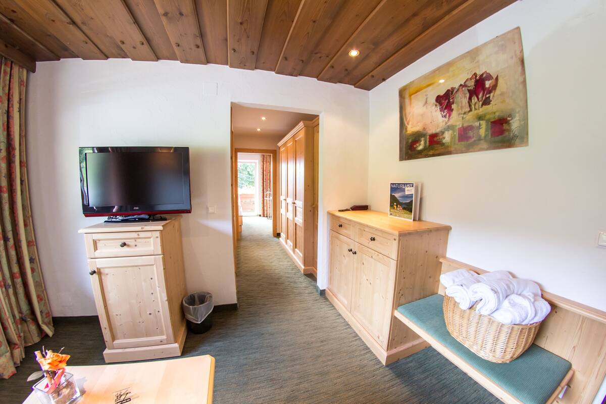 Une chambre d’hôtel avec un téléviseur posé sur un meuble en bois, un panier en osier contenant des serviettes et un tableau accroché au mur.