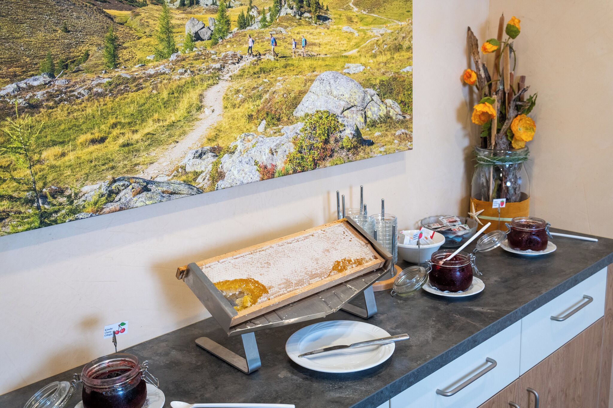 Un buffet est installé sur un comptoir, avec un plateau de nourriture, des pots de confiture et un vase rempli de fleurs.