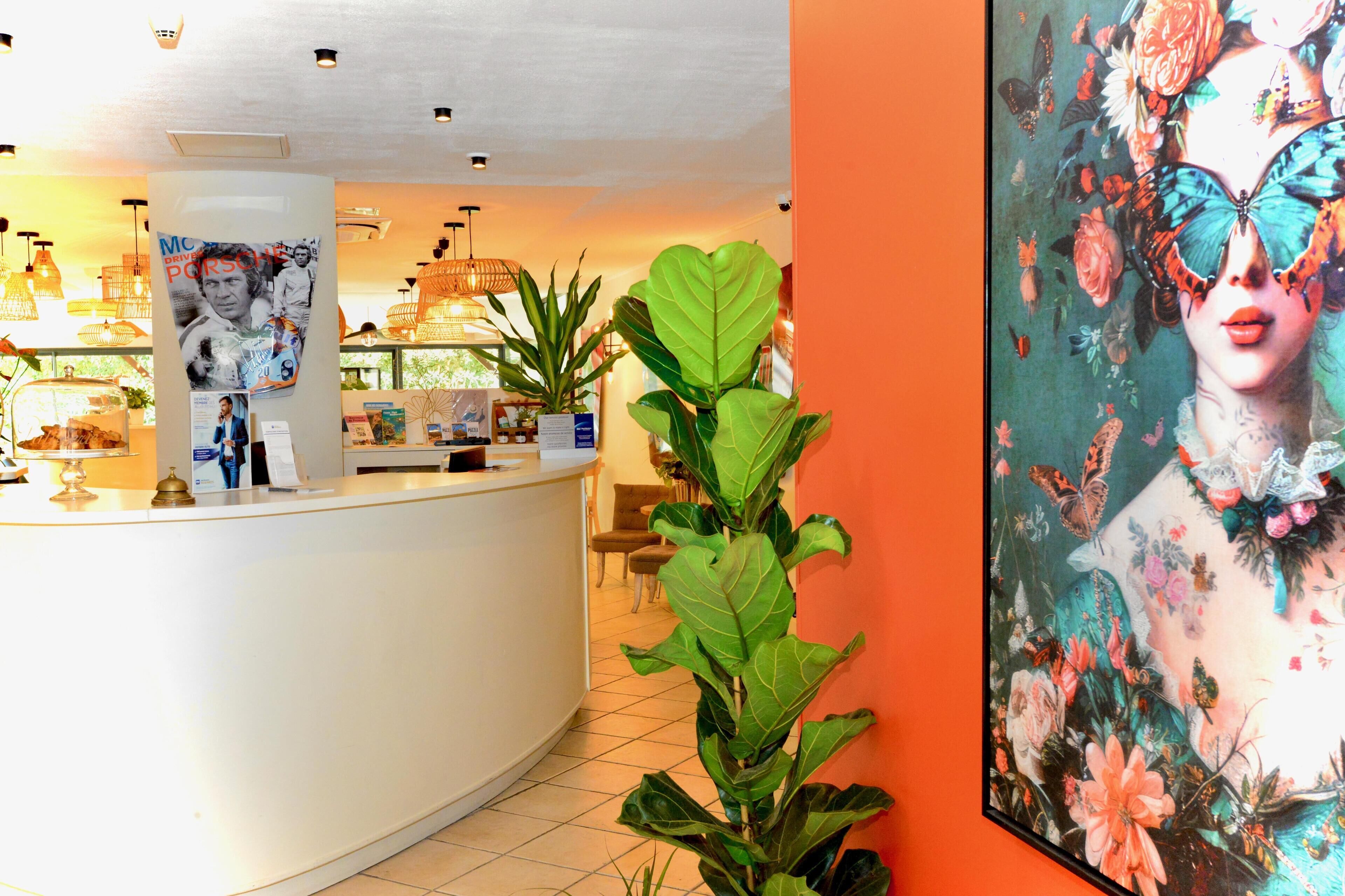 Una zona de recepción con un mostrador blanco, un cartel grande de una mujer con mariposas y una planta en maceta.