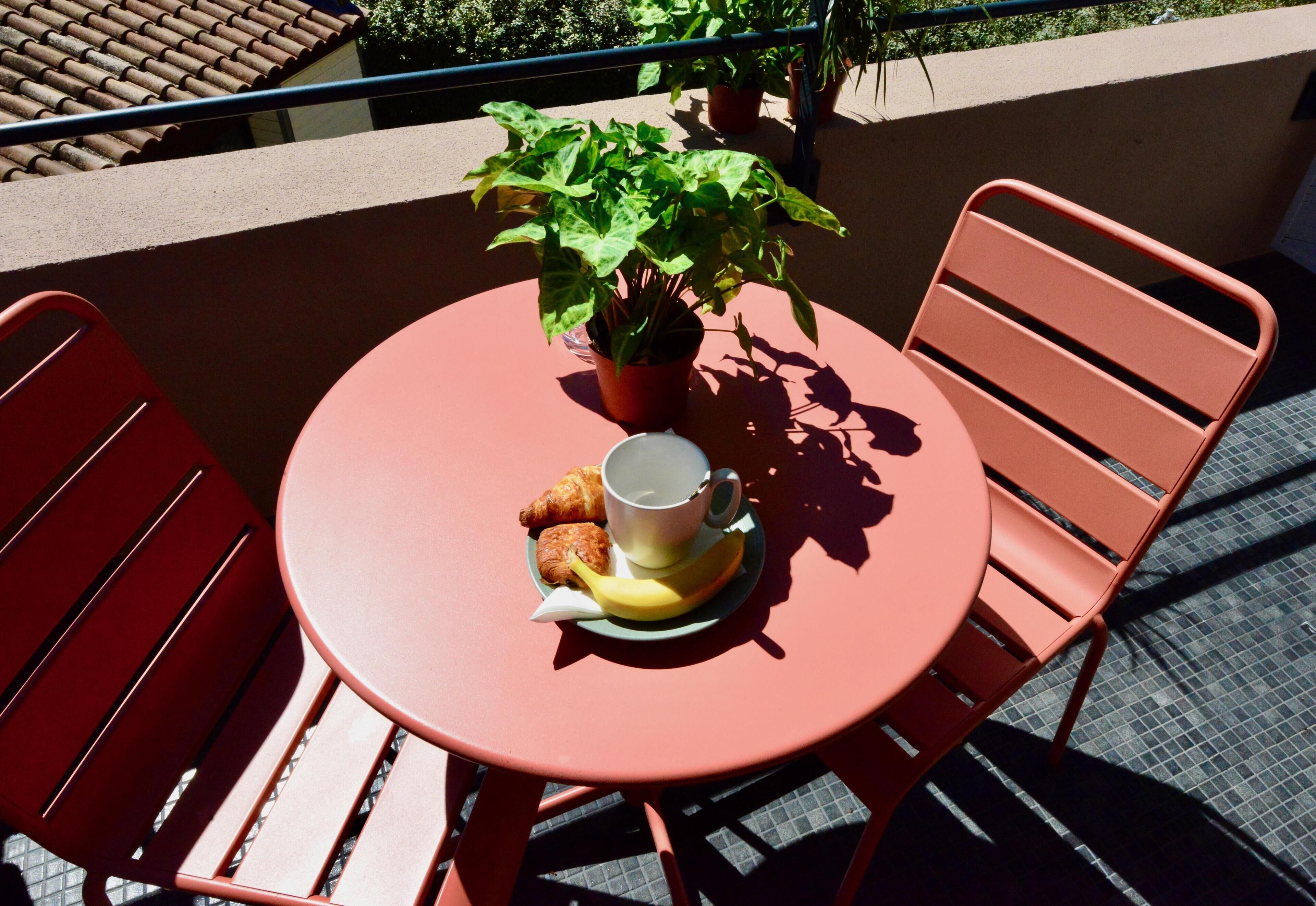 Una mesa redonda con una planta en maceta, una taza, un croissant y un plátano sobre un mantel rojo.