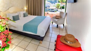 Une chambre d’hôtel avec un lit, une chaise, une valise rouge et un chapeau posé sur la table.