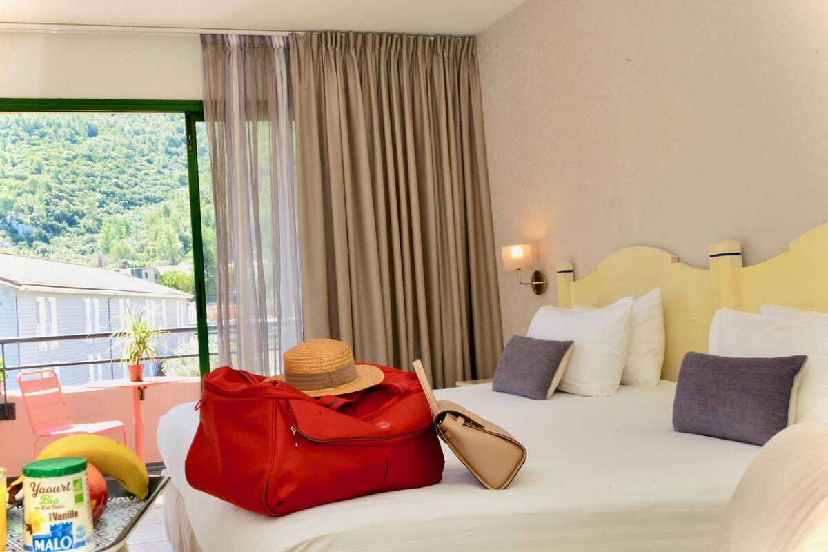 Een hotelkamer met een bed, een koffer, een hoed, een fles melk en een banaan op een tafel.