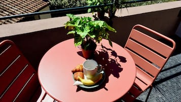 Una mesa redonda con una planta en maceta, un croissant, una taza y un plátano sobre un mantel rojo.
