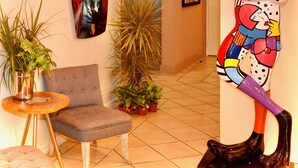 Un hall d’entrée avec un fauteuil gris, une plante en pot, un luminaire fixé au mur et une affiche de voiture.