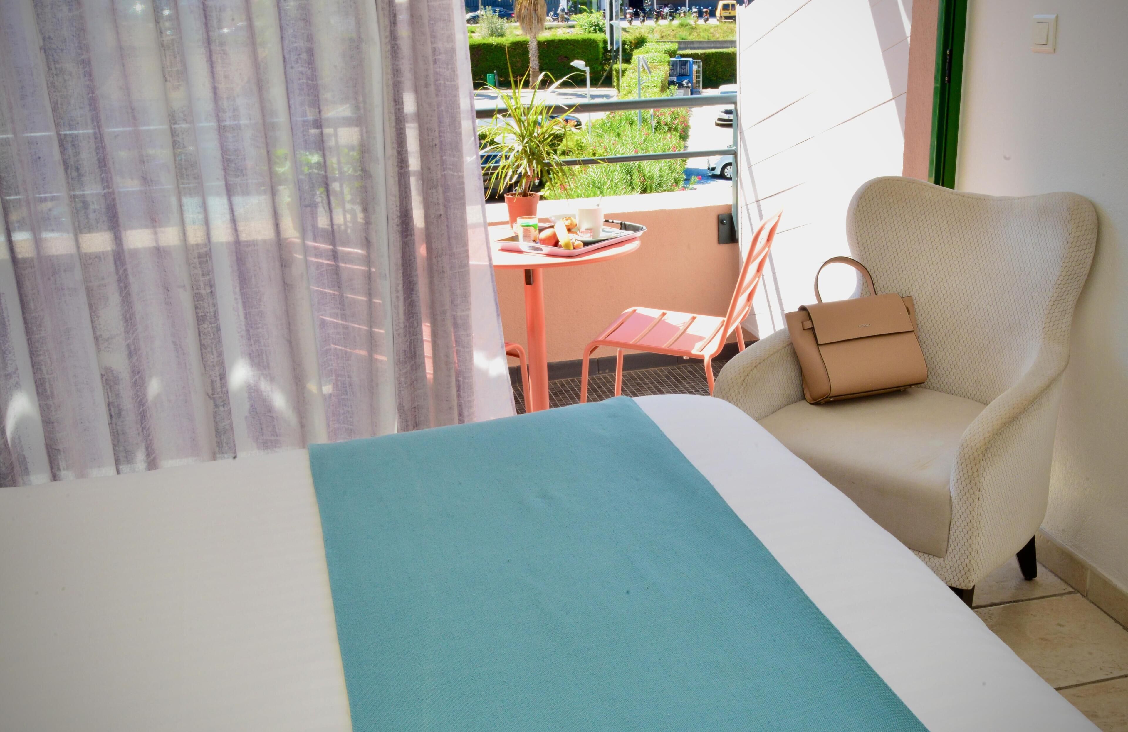 Une pièce avec un lit, une chaise, une table avec une plante et une vue sur l’extérieur.