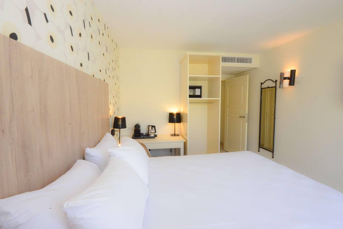 Een hotelkamer met een bed, nachtlampjes, een bureau met telefoon, een spiegel en een kledingkast.