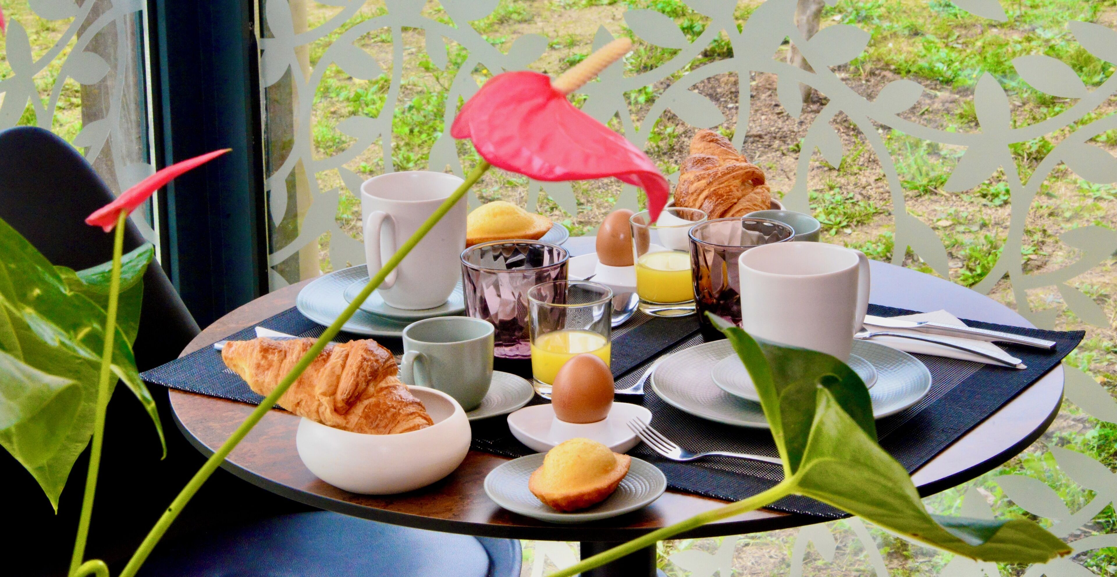 Mesa de café da manhã com croissants, ovos, suco e xícaras de café.