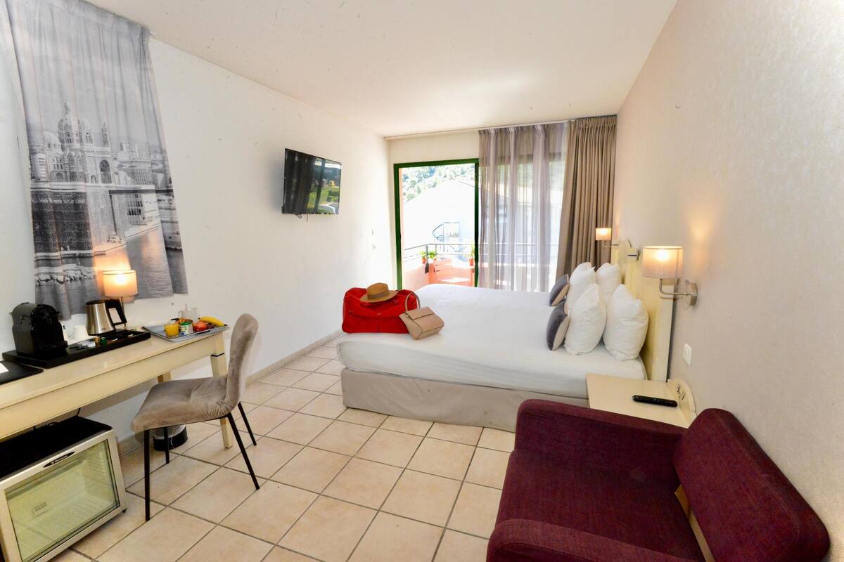 Een hotelkamer met een bed, een bureau met een computer, een stoel, een aan de muur bevestigde televisie en een raam met gordijnen.