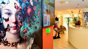 Un hall d’hôtel agrémenté d’une grande fresque florale, d’un panneau d’information vert et d’un comptoir de réception orné d’une plante en pot.