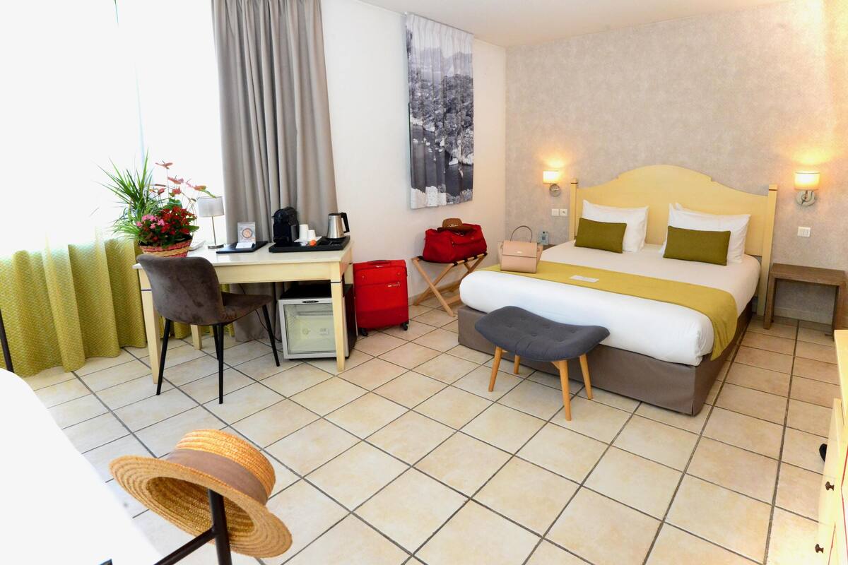 Een hotelkamer met een bed, bureau, stoel en een klein tafeltje met een plant.