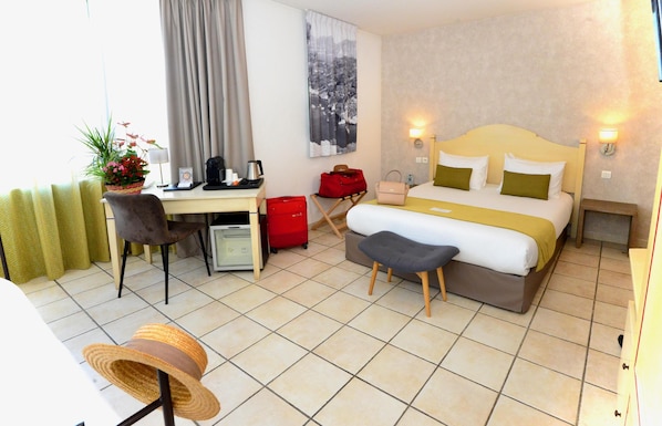 Habitación de hotel con cama, escritorio, silla y una pequeña mesa con una planta.