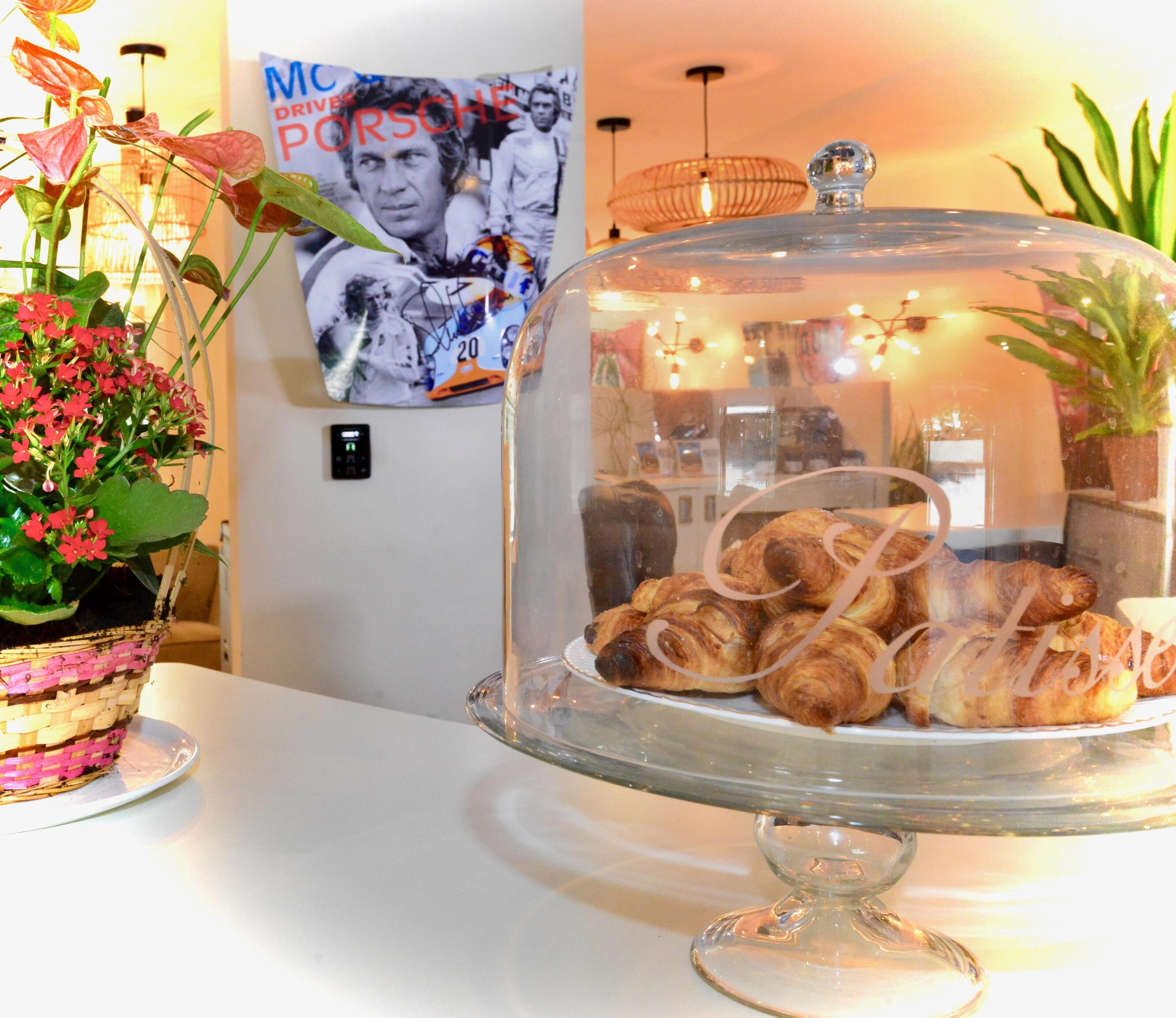 A glass display case with croissants, a wicker basket with flowers, and a poster on the wall.