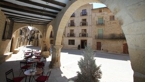 Un café en plein air avec des tables et des chaises, des arches en pierre et, au fond, un bâtiment doté de balcons.