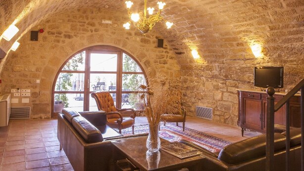 Une pièce chaleureuse avec un plafond en pierre, une grande fenêtre en arc de cercle, des fauteuils en cuir, un lustre et un téléviseur à écran plat.