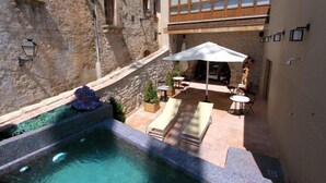 Un espace piscine agrémenté d’un mur en pierre, de chaises longues et d’une table avec un parasol.