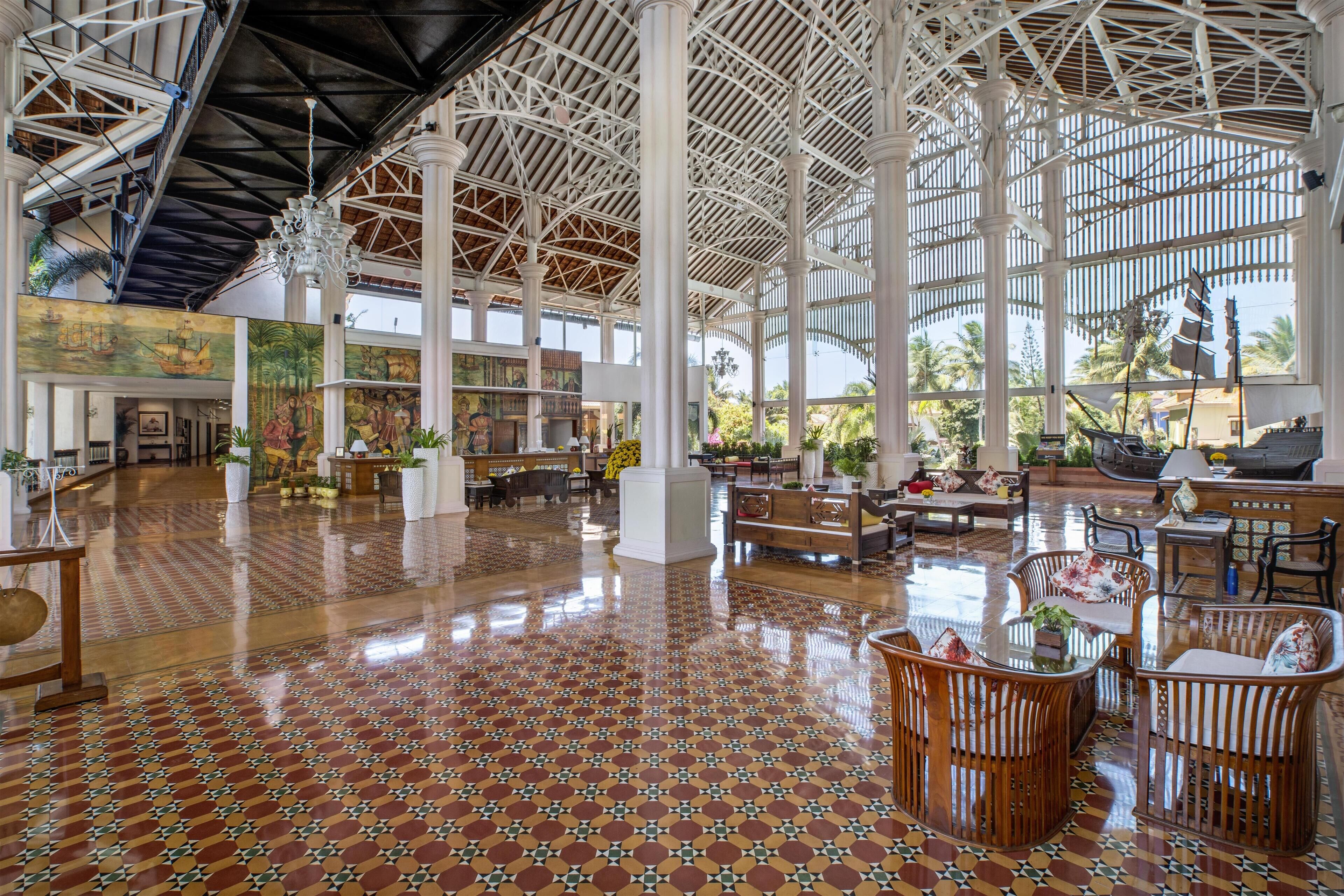 A spacious lobby with a high ceiling, patterned floor tiles, and a central seating area with tables and chairs.