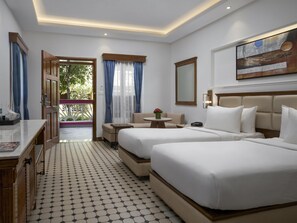 A hotel room with two beds, a desk, a chair, and a small table with a vase of flowers. - Radisson Blu Resort Goa Cavelossim Beach (Cavelossim)