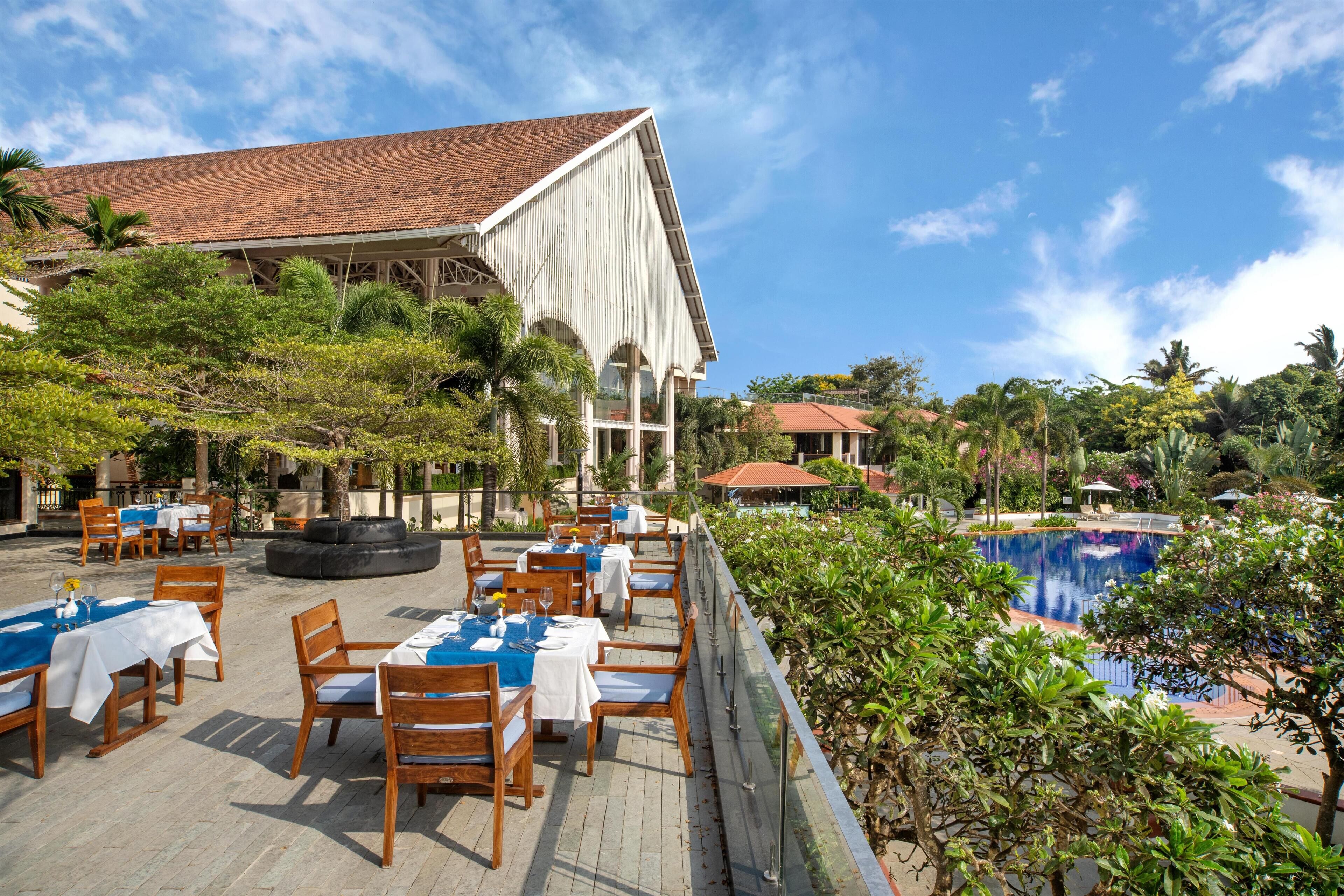 An outdoor dining area with tables and chairs, a pool, and a building with a tiled roof.