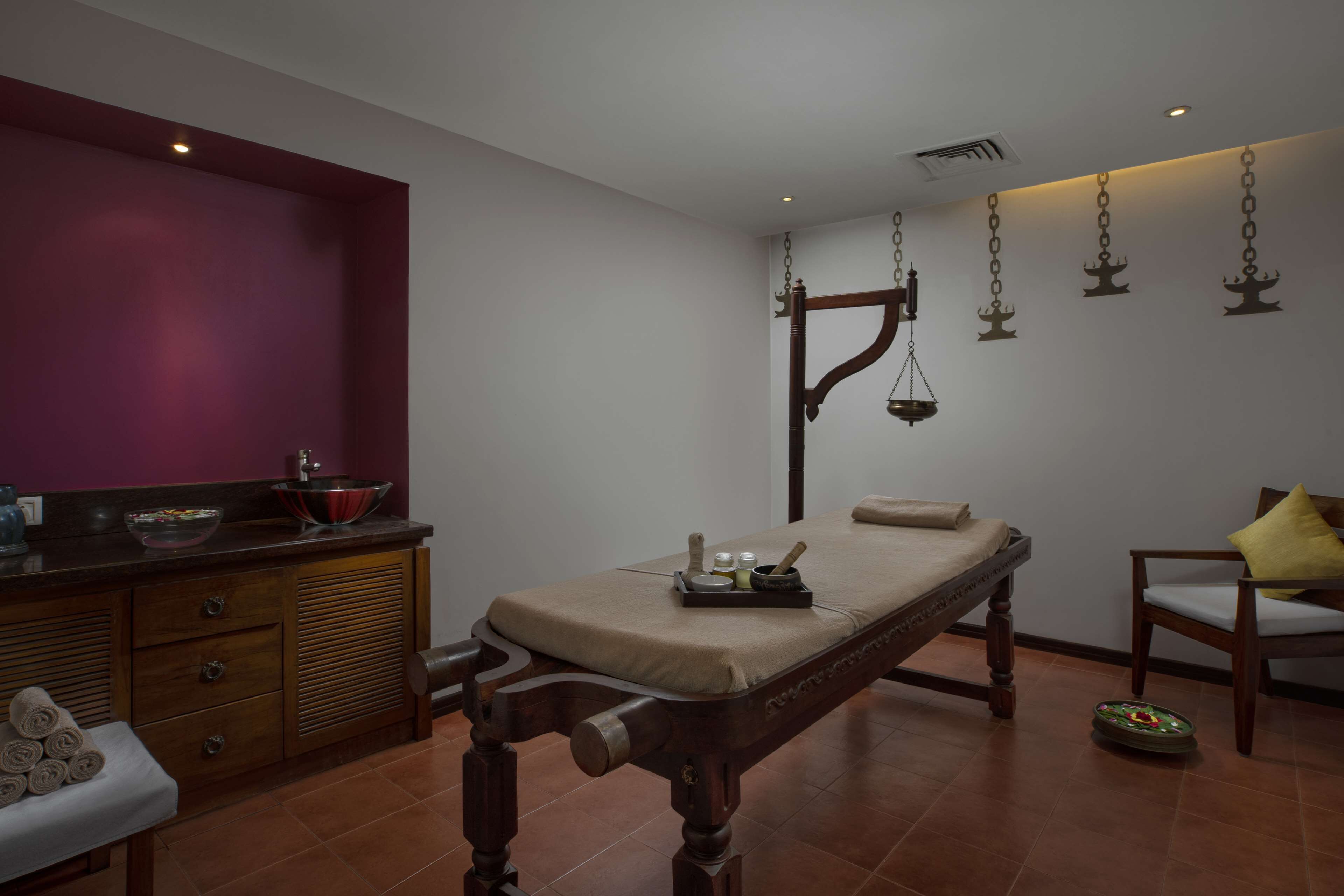 Une chambre traditionnelle avec un lit en bois, une petite table sur laquelle se trouvent un bol et un lavabo, une chaise avec un coussin et une balance suspendue.