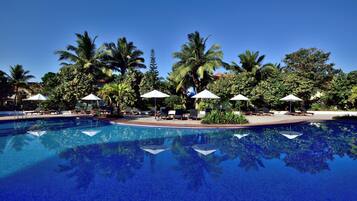 A clear blue pool with lounge chairs and umbrellas, surrounded by palm trees and greenery.