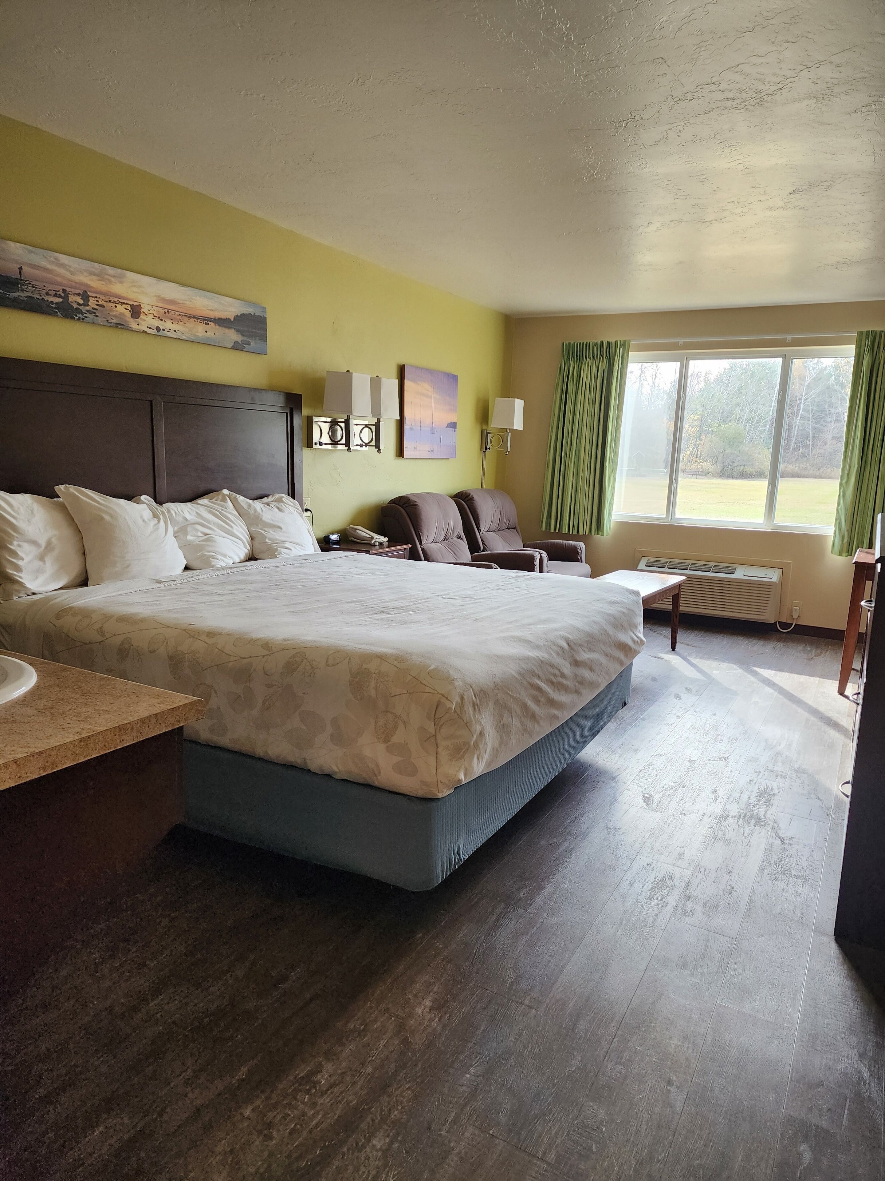 Une chambre d’hôtel avec un grand lit, un bureau, une chaise, une fenêtre avec des rideaux et des œuvres d’art accrochées au mur.