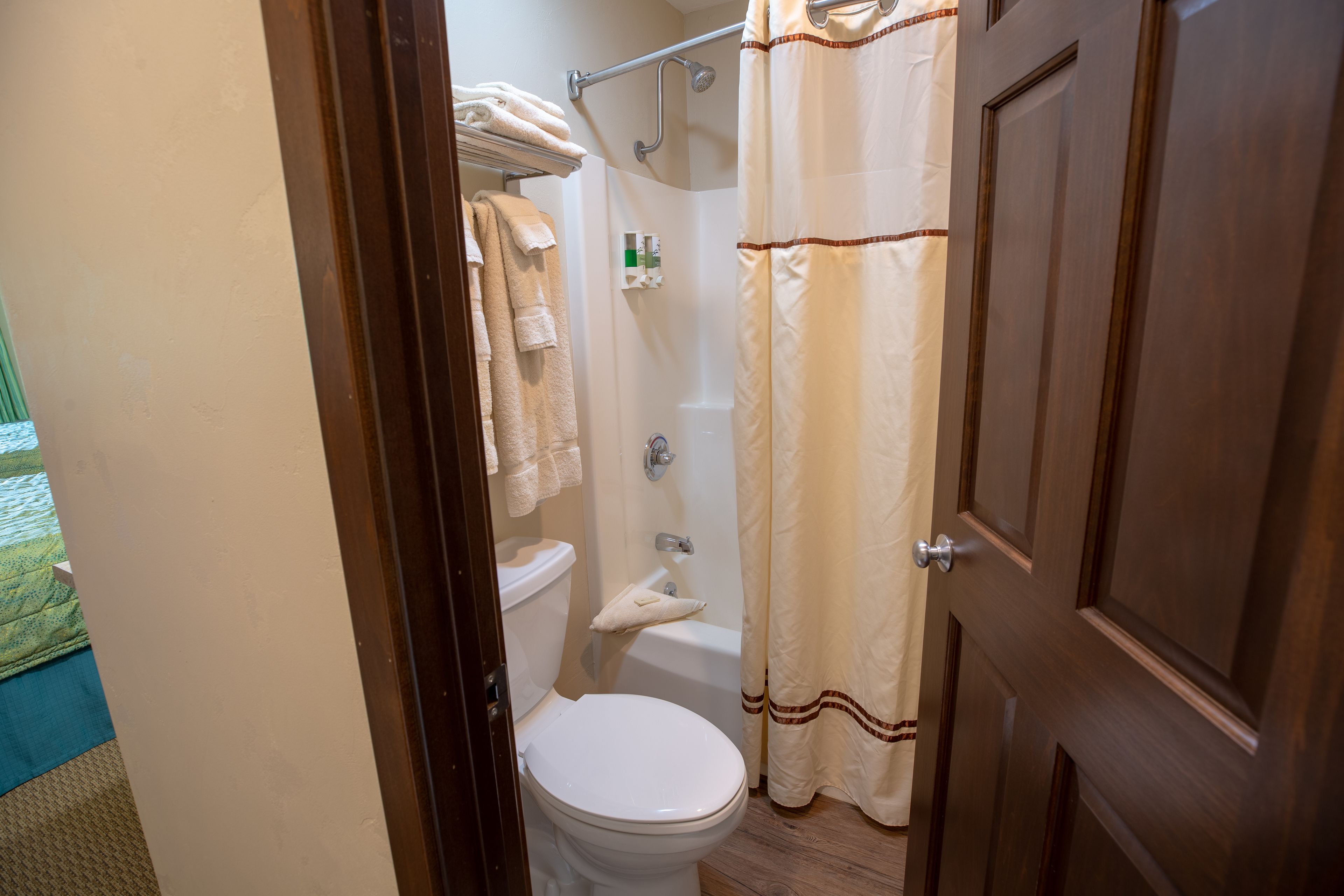 Un baño con inodoro, ducha y bañera. Hay toallas en un estante sobre el inodoro.