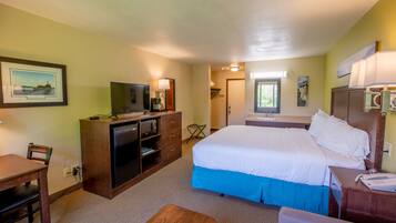 A hotel room with a bed, desk, television, and a window with a view of trees.