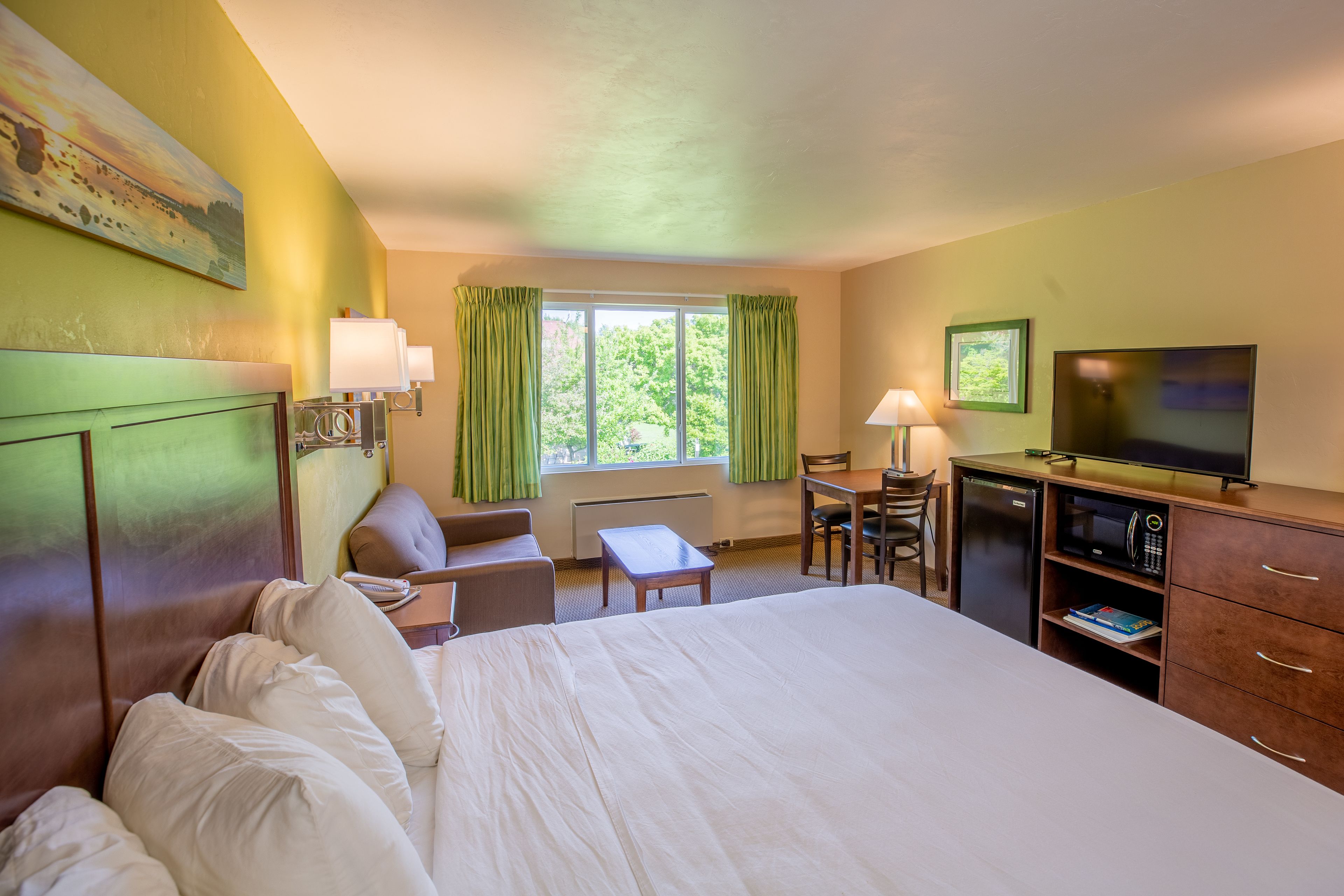 A hotel room with a large bed, a desk with a chair, a television, and a window with curtains.