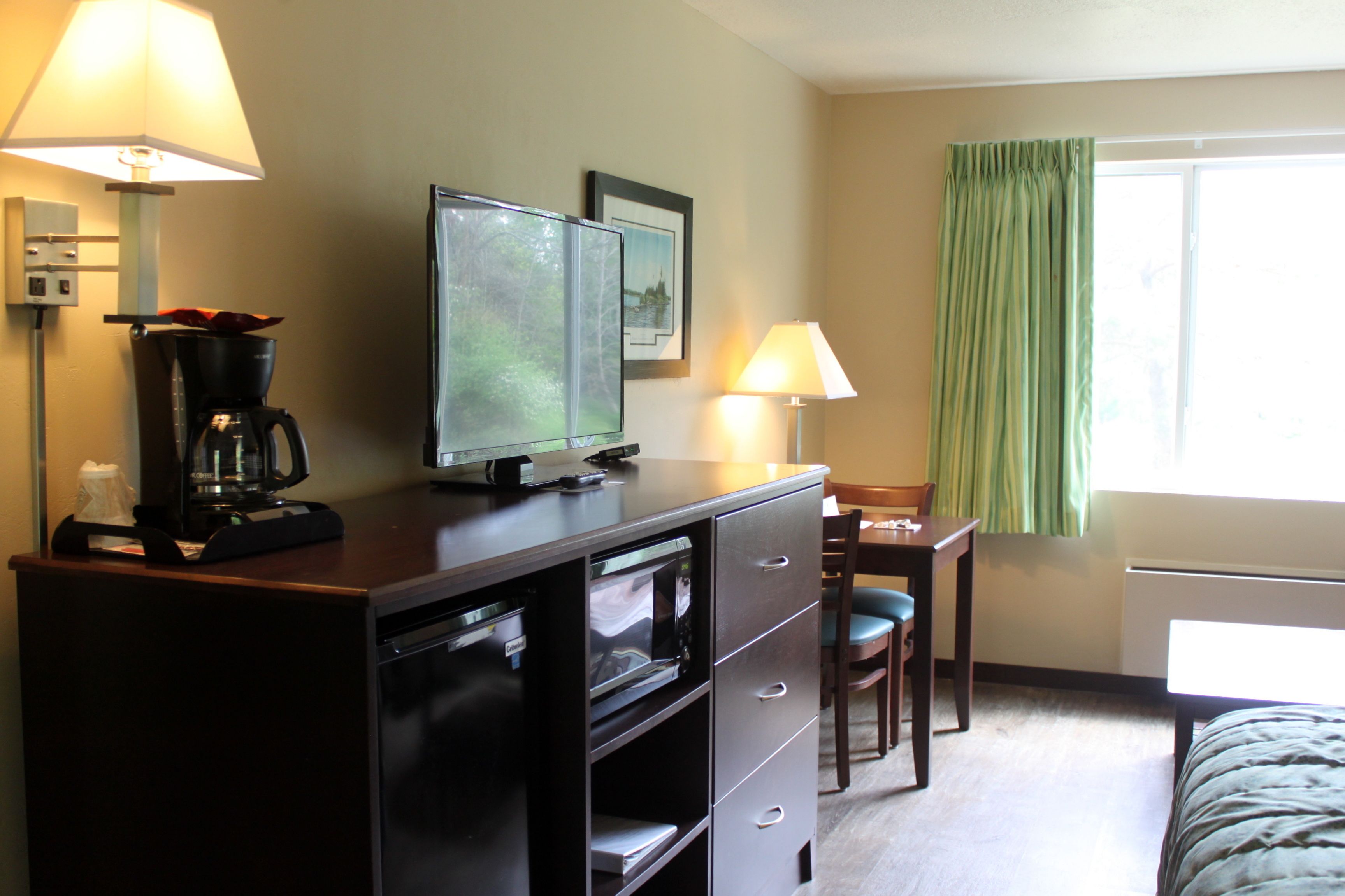 A hotel room with a bed, a desk with a chair, a coffee maker, a television, and a window with curtains.