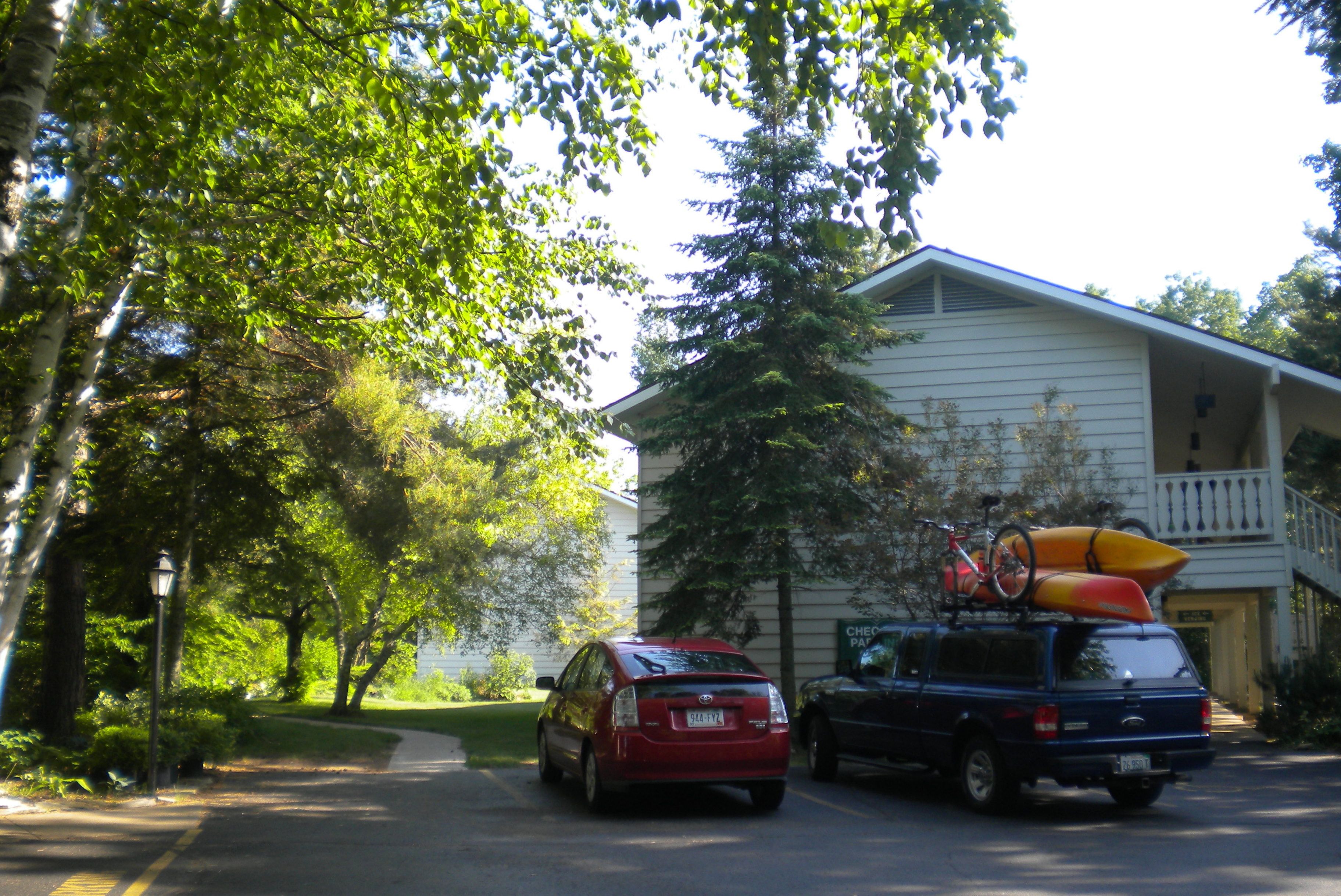 A two-story house with a garage, parked cars, and kayaks on the roof.