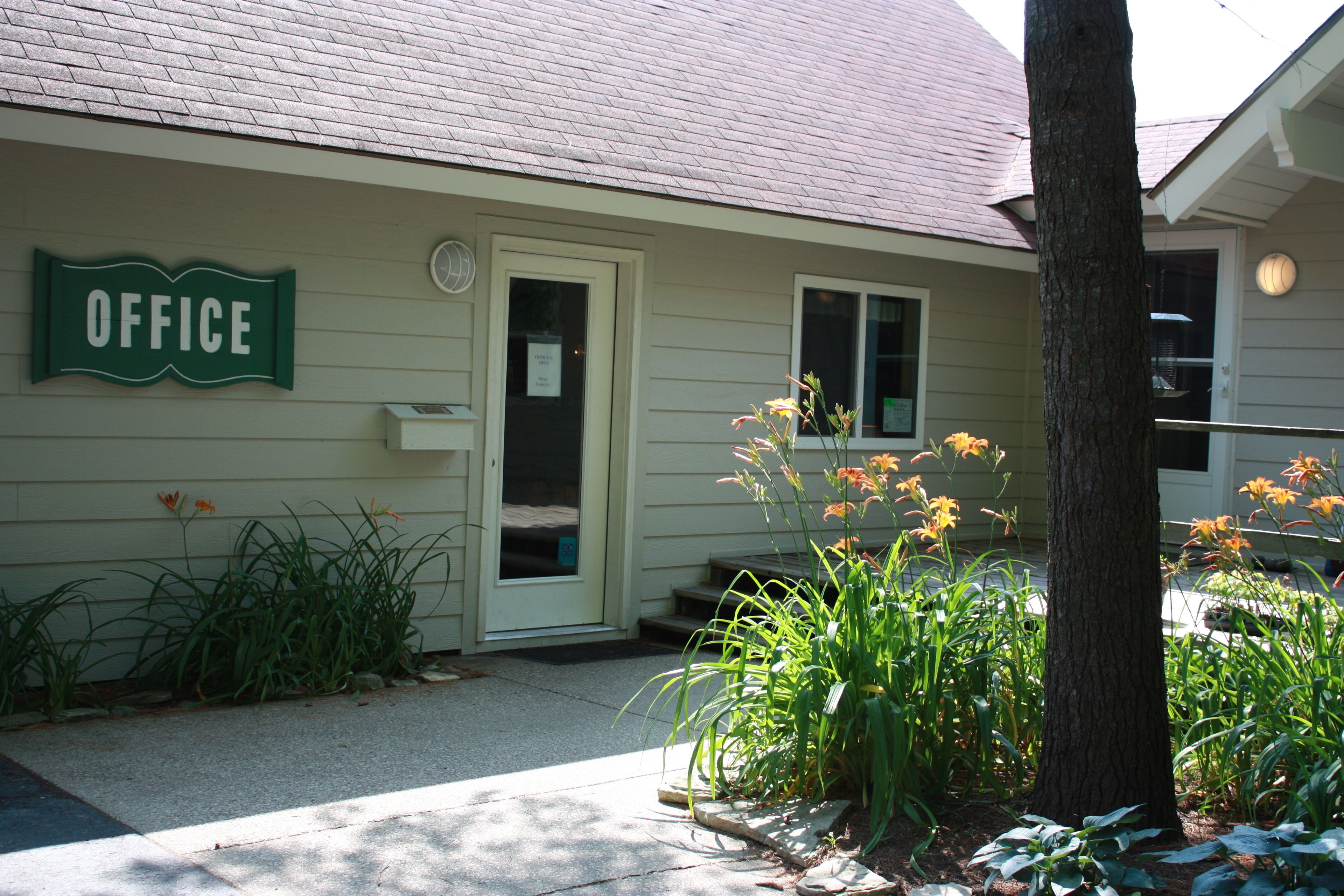 A building with a sign reading "OFFICE" on the side, a door, and a small porch area with plants.