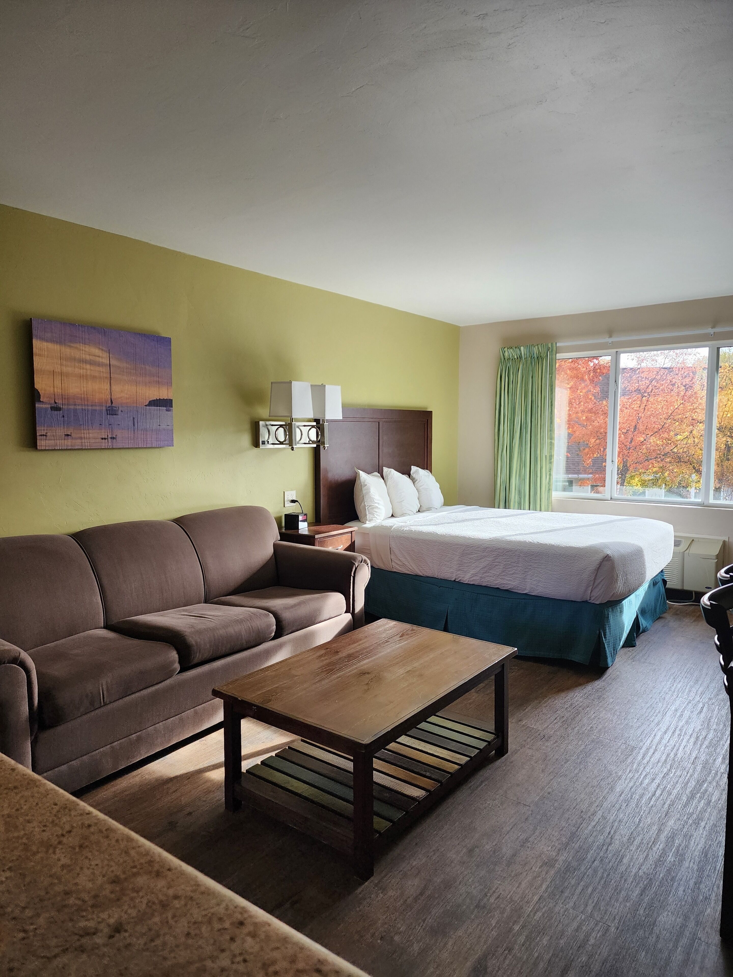 A hotel room with a bed, a sofa, a coffee table, and a painting on the wall.
