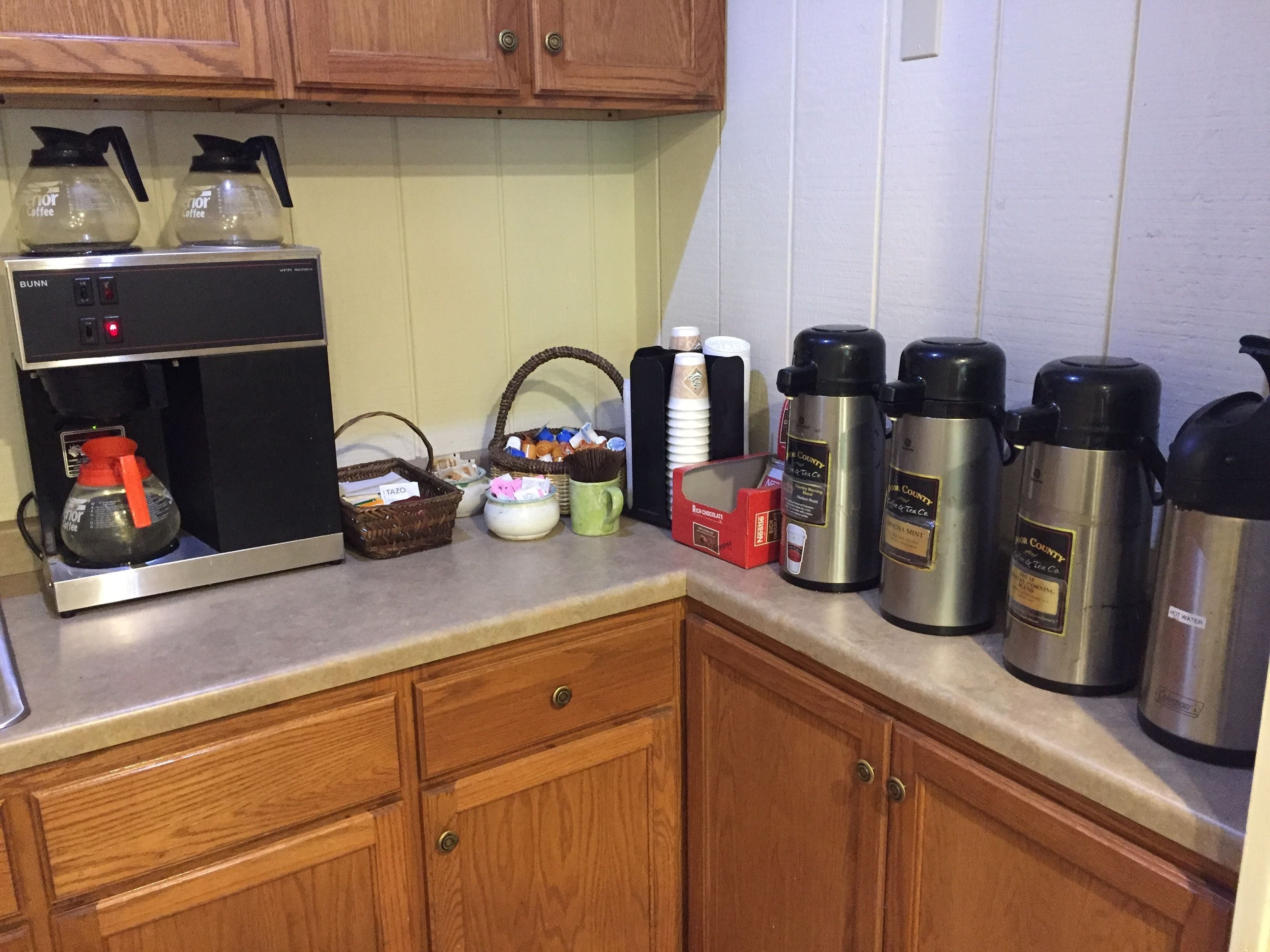 Une cuisine équipée d’une machine à café, de thermos et de différents récipients posés sur le plan de travail.