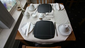 A dining table set with white plates, silverware, and a black placemat. - The Tennyson (Bridlington)