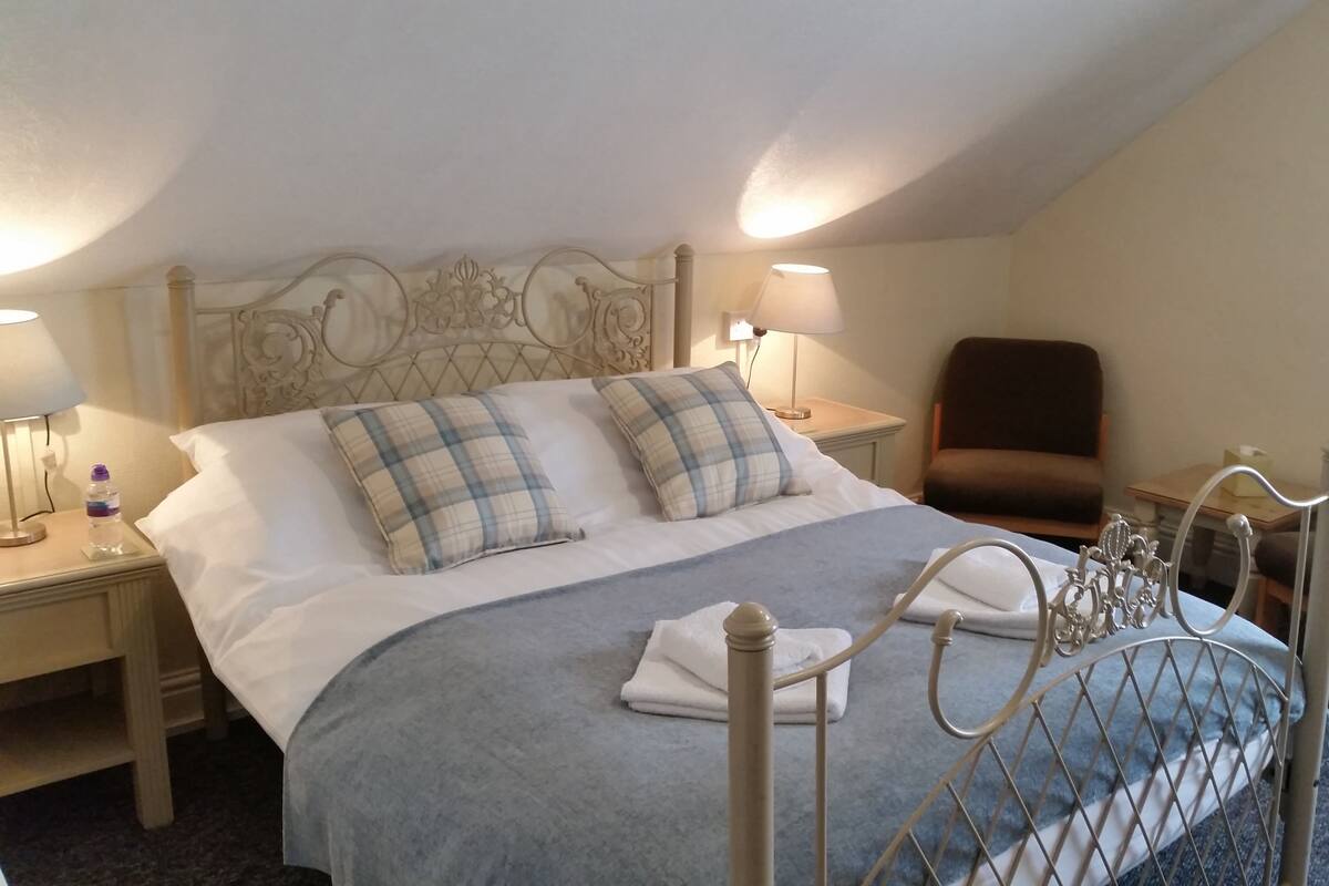 A hotel room with a large bed, two bedside lamps, a chair, and a nightstand with a water bottle.