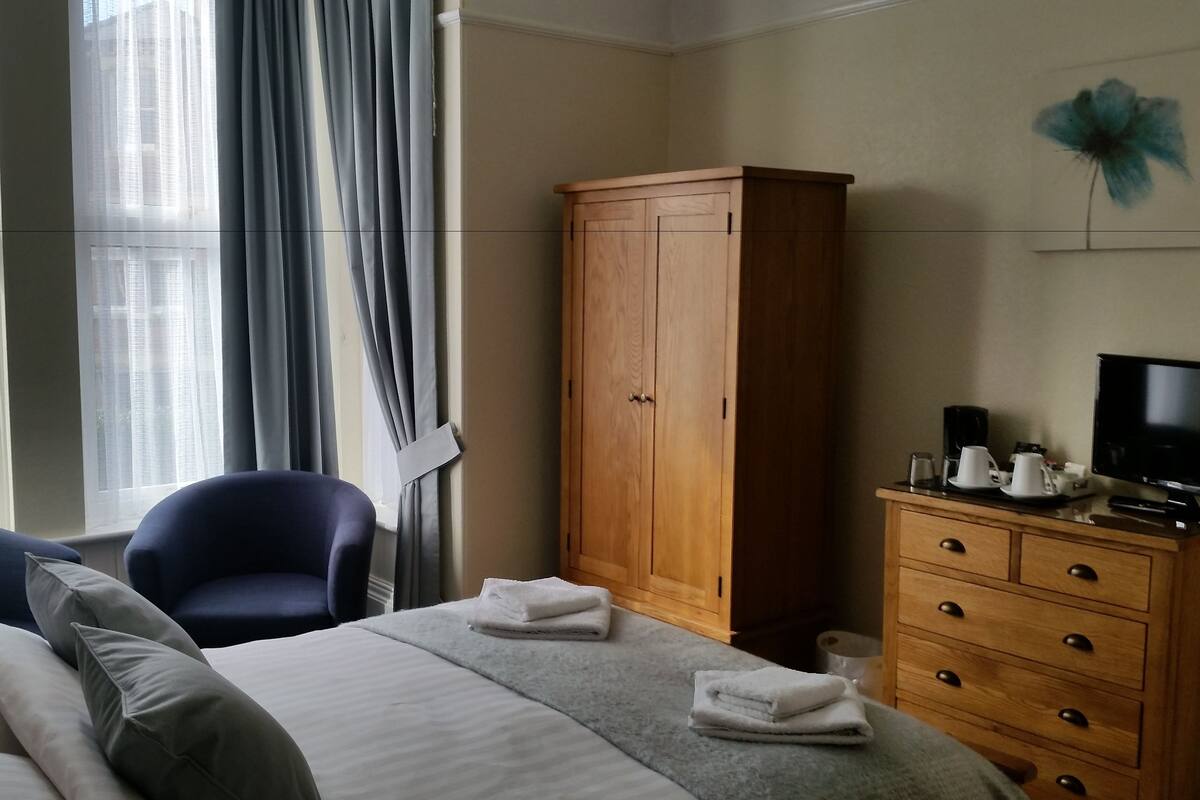 A hotel room with a bed, a chair, a wardrobe, a television, and a coffee maker.
