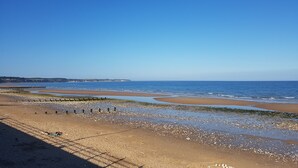 A beach with a wooden pier extending into the sea, clear skies, and distant cliffs. - The Tennyson (Bridlington)